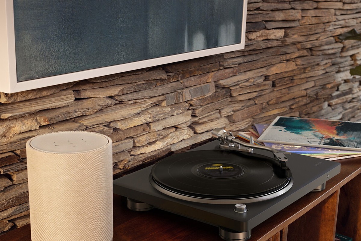 Kleiner hellbeiger kabelloser Lautsprecher neben einem Plattenspieler und Schallplatten