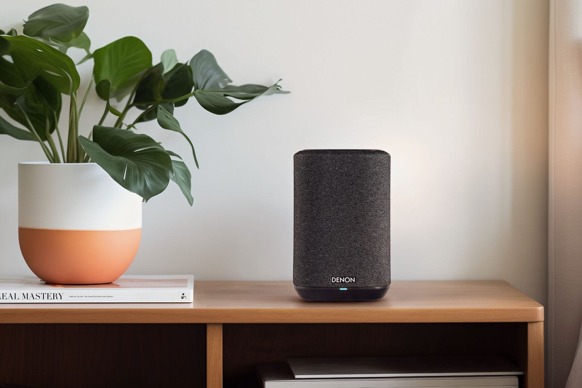 Compact black wireless speaker on a wooden cabinet, next to a plant