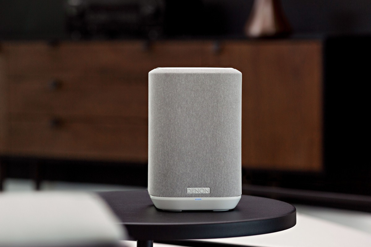 Small white speaker on a black side table, wooden furniture in the background