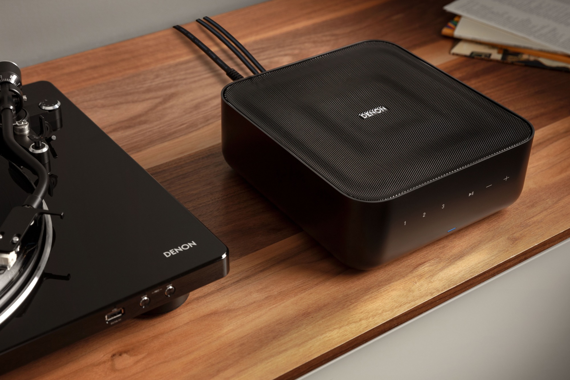 Amplificatore compatto nero su un mobile in legno, accanto a un giradischi