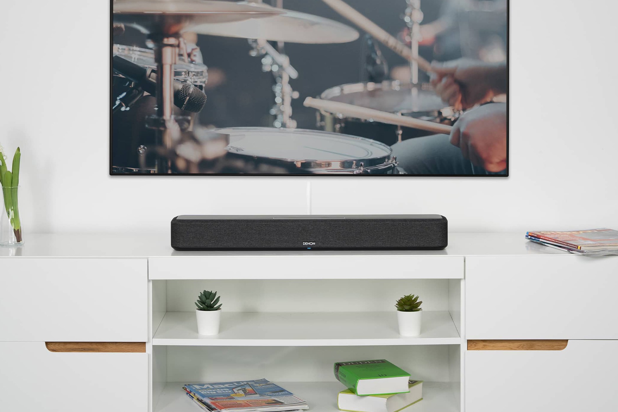 Kompakte Soundbar auf einem weissen TV-Möbel, unter einem Wandfernseher