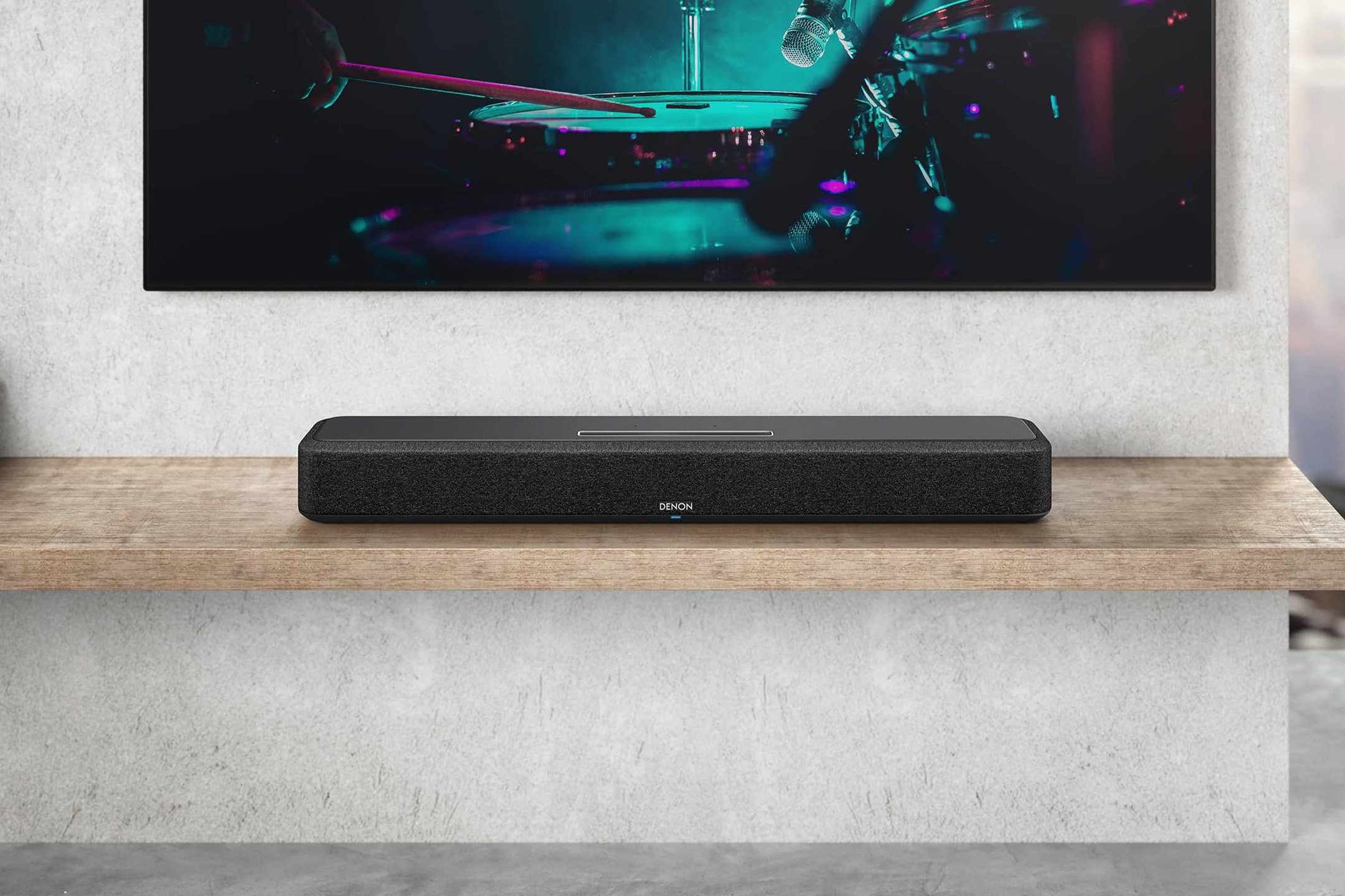 Soundbar auf einem Holzboard, unter einem Fernseher an einer Betonwand