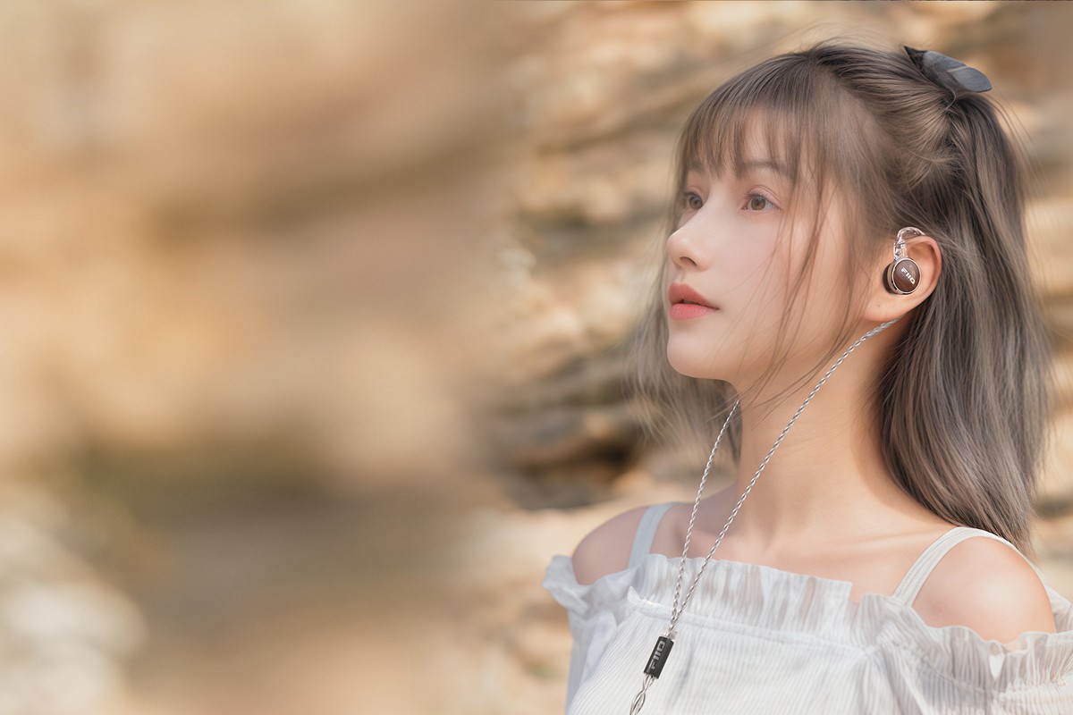 Jeune femme portant un écouteur intra-auriculaire relié à un câble argenté