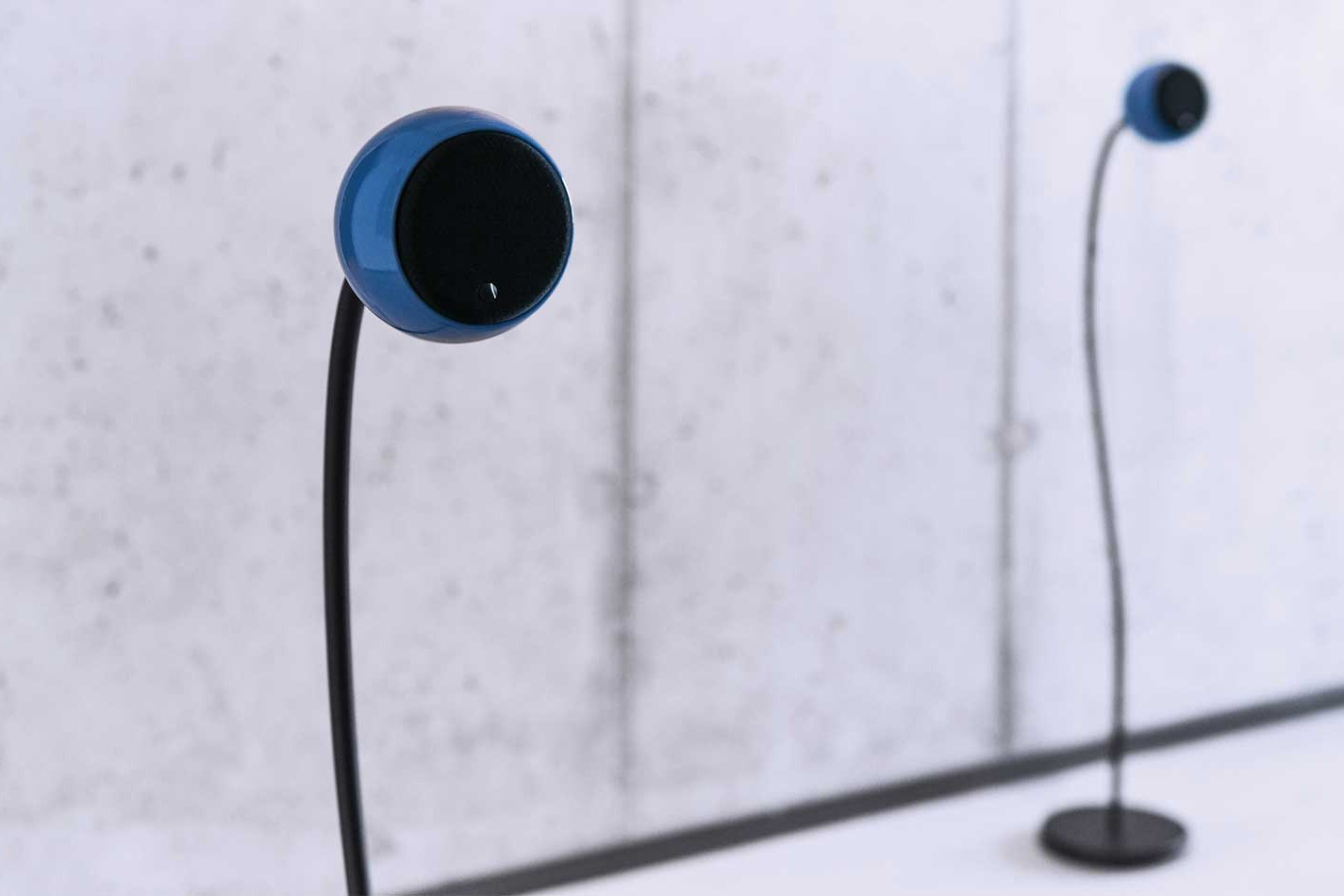 Enceinte bleue sur un pied fin devant un mur en béton