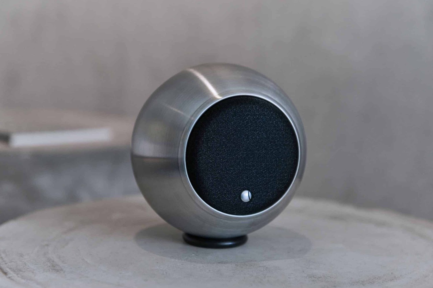 Enceinte argentée à grille noire posée sur un guéridon en bois