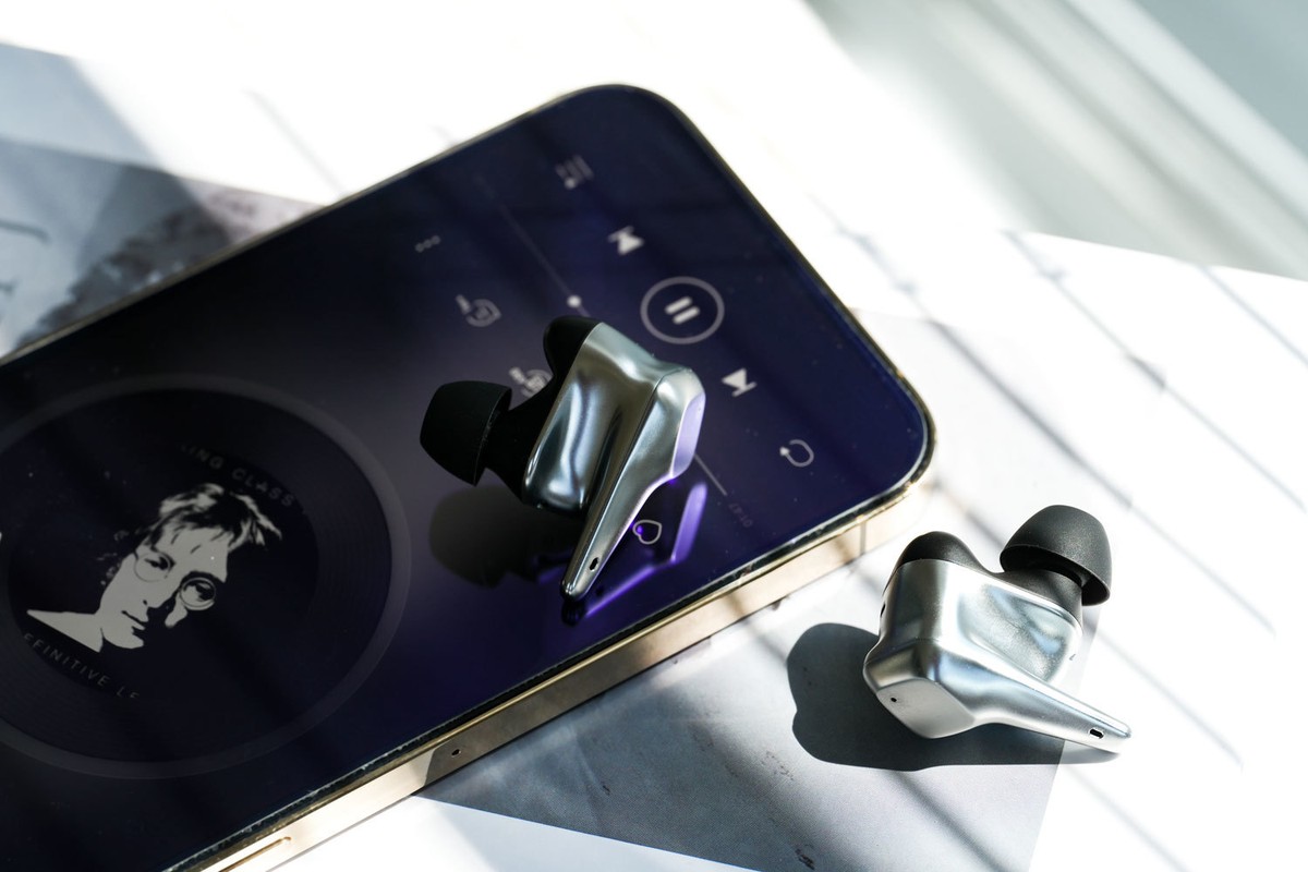 Silver earbuds resting on a smartphone with its music player open