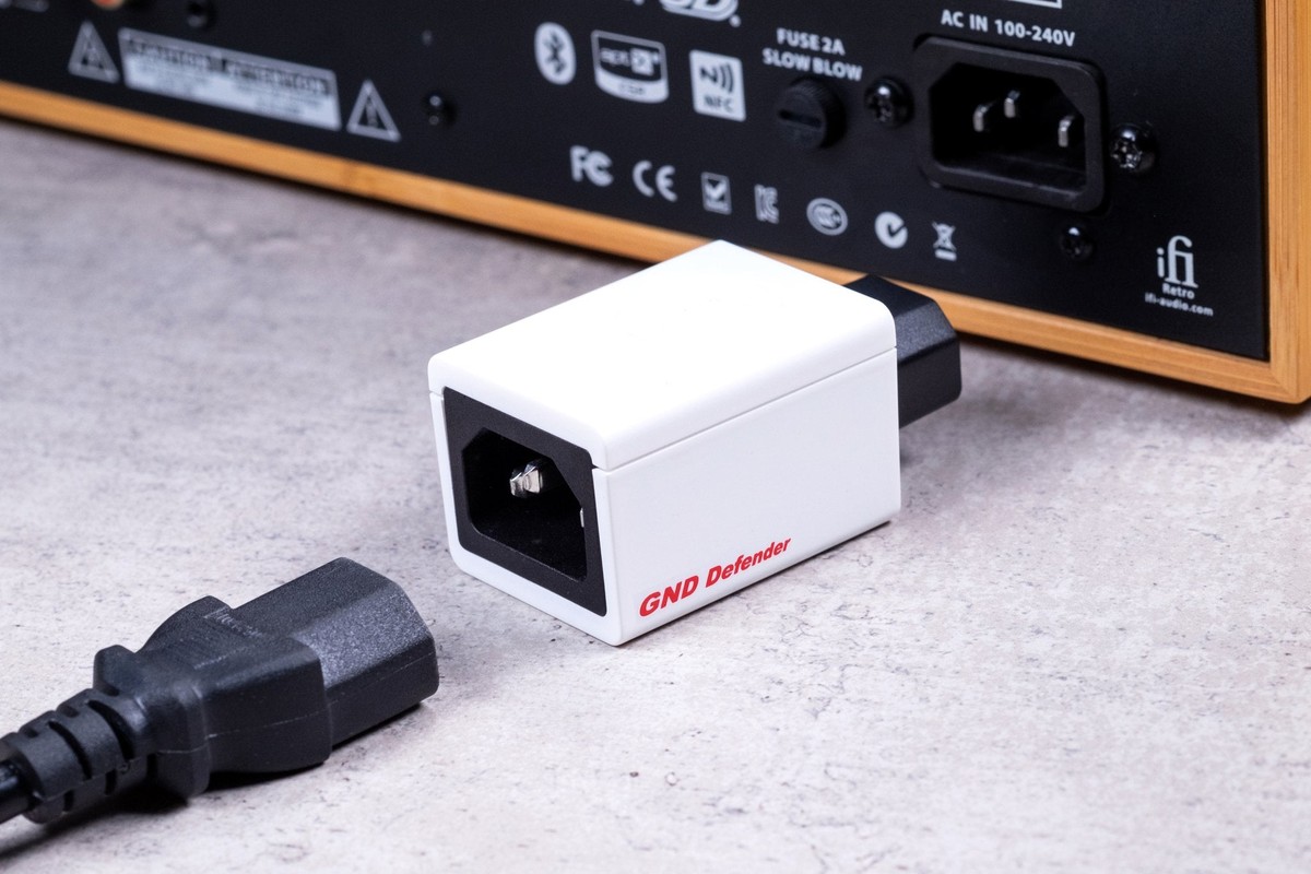 Piccolo modulo bianco collegato al retro di un apparecchio audio, cavo di alimentazione a terra