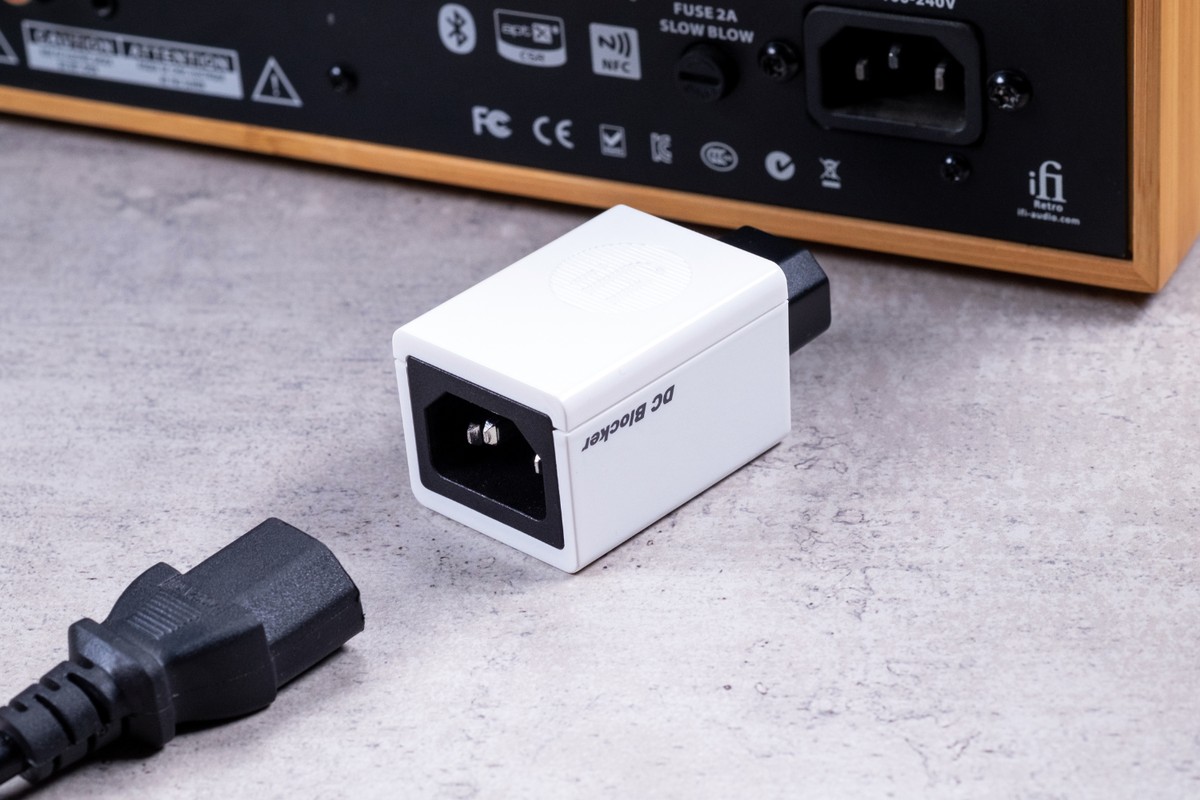 White unit plugged into the back of an audio component, black mains lead in the foreground