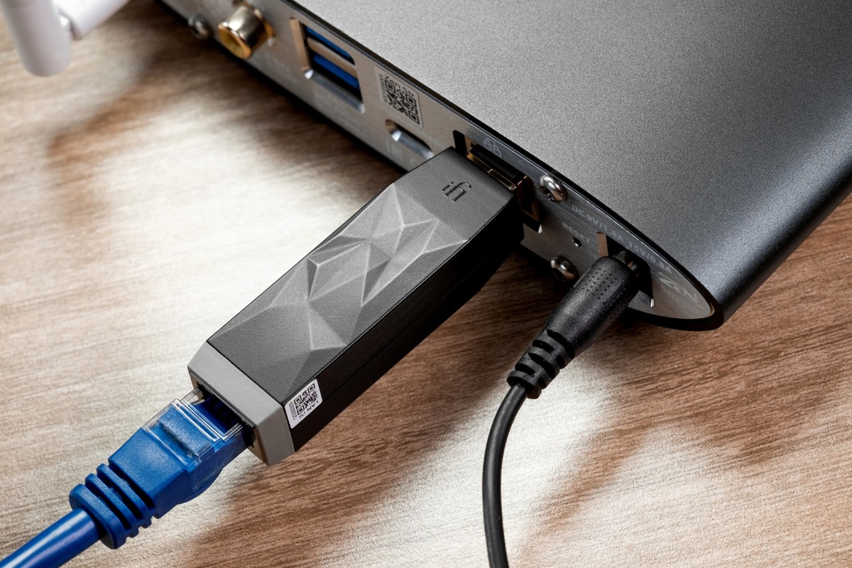 Schwarzer Filter im Netzwerkanschluss eines Geräts, blaues Ethernet-Kabel, auf einem Holztisch