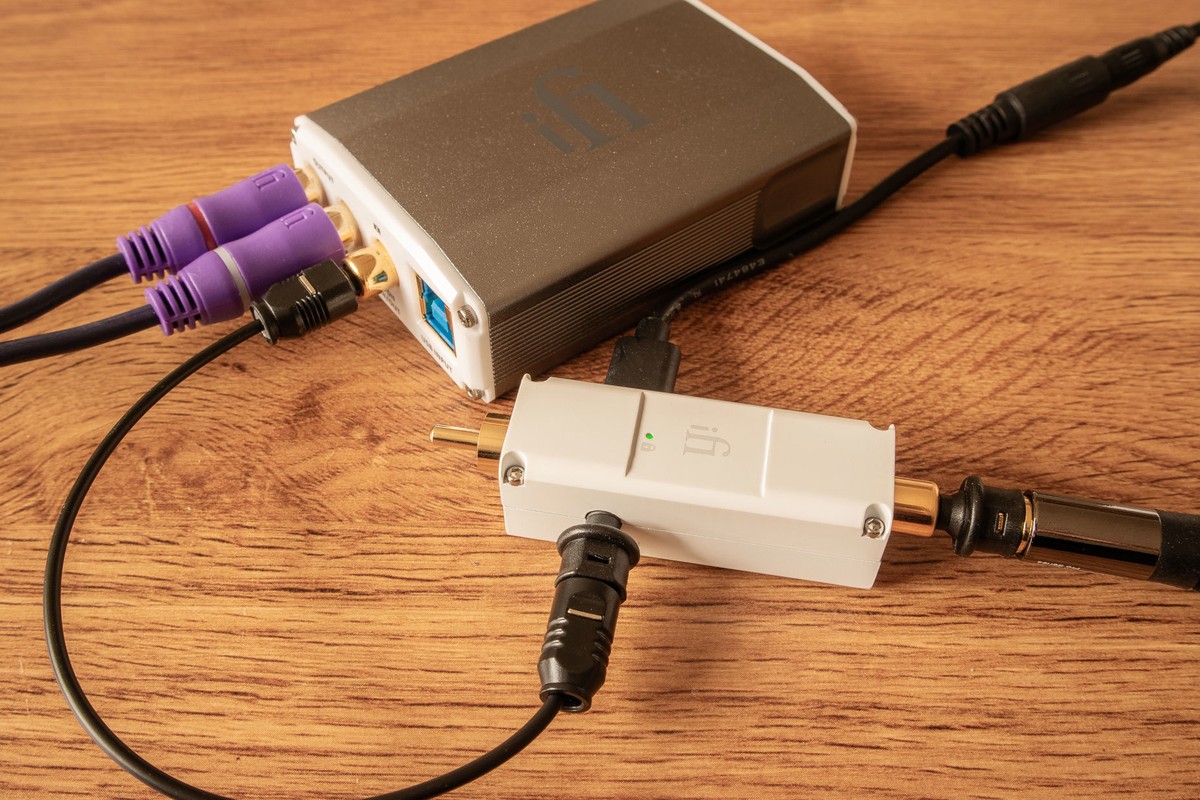 Petit boîtier blanc relié à un DAC par des câbles coaxial et optique, sur une table en bois