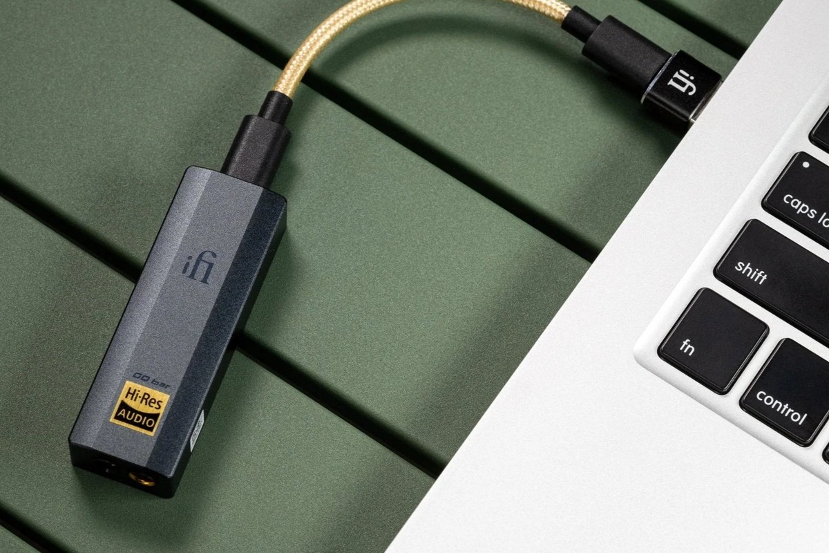 Small grey DAC linked by a gold cable to a laptop, on a green table