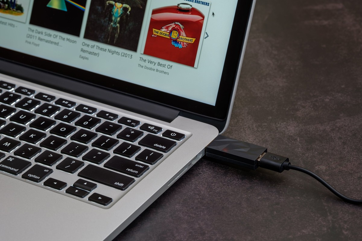 Small black filter plugged into the side of a laptop, black cable
