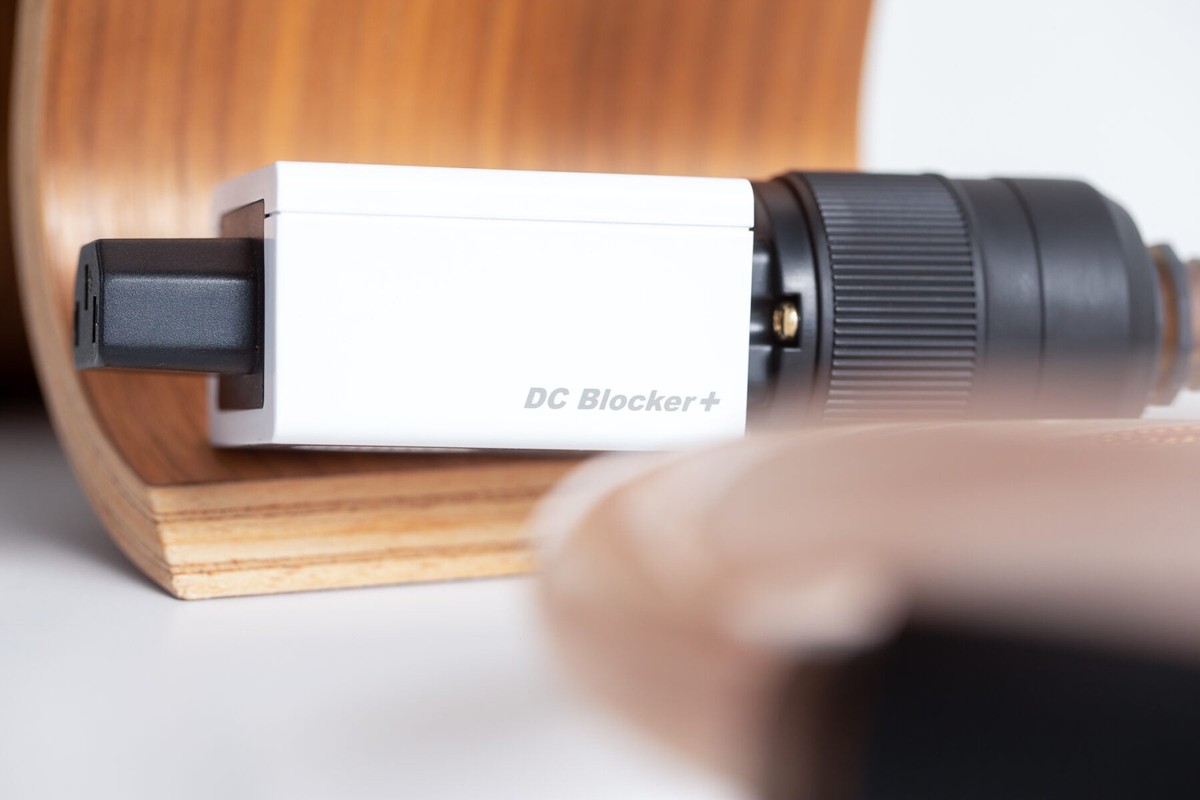 Weisser Adapter an einem massiven Netzstecker, auf einer hellen Holzunterlage