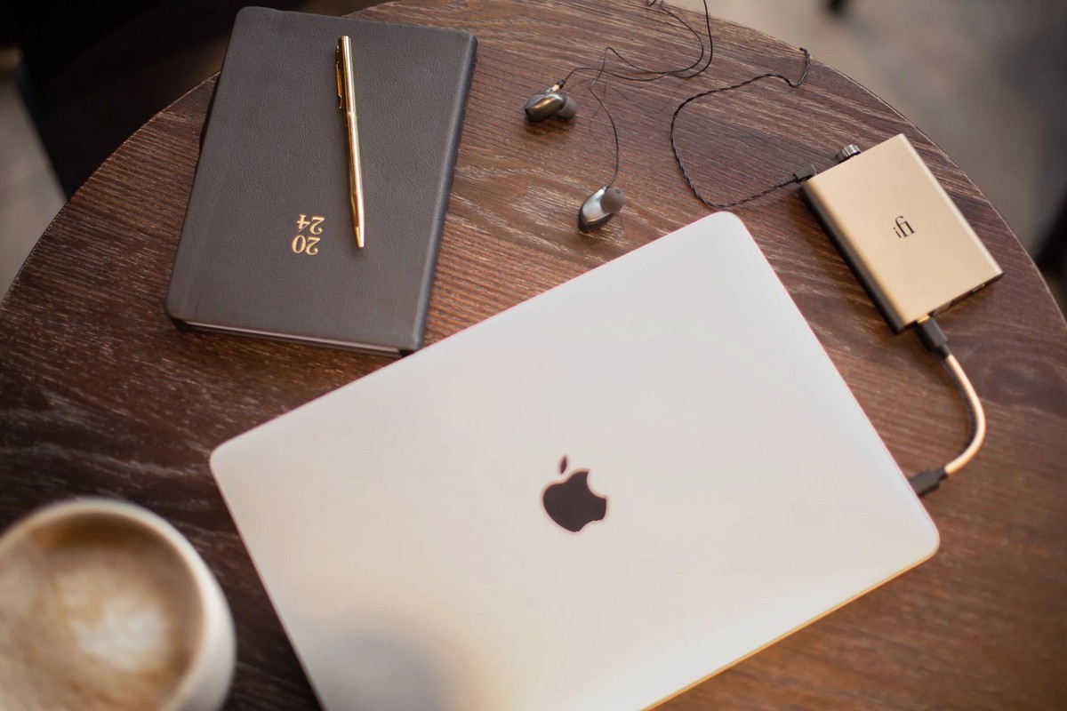 Top view of a café table with a laptop, a notebook and earphones linked to the gold unit