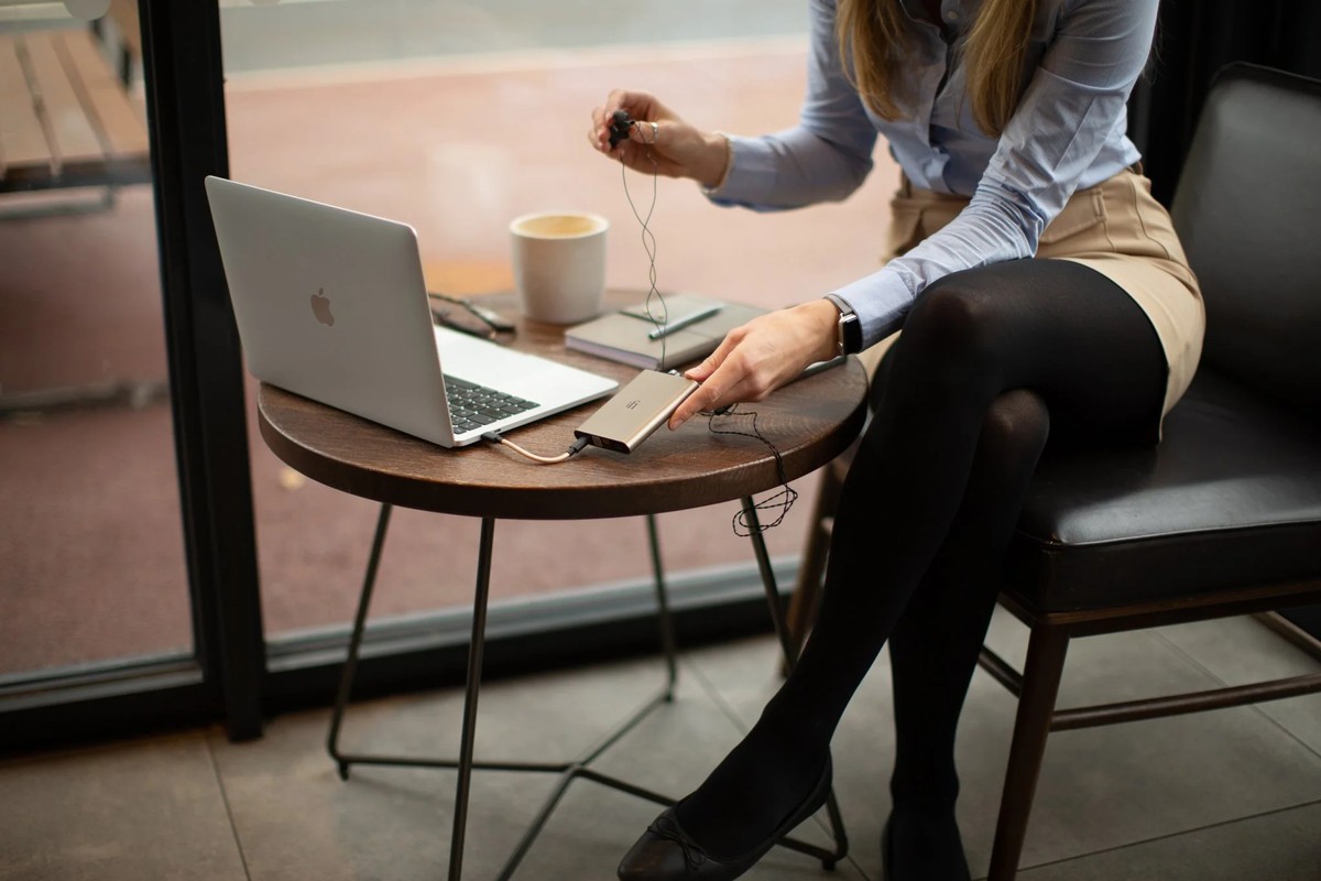 Woman seated on a terrace plugging in her earphones, laptop and cup on the table