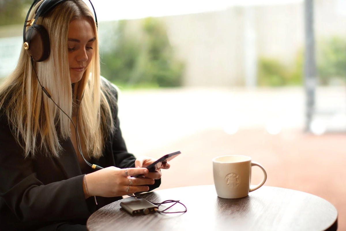 Young woman wearing headphones and checking her phone, the DAC on the table next to a coffee