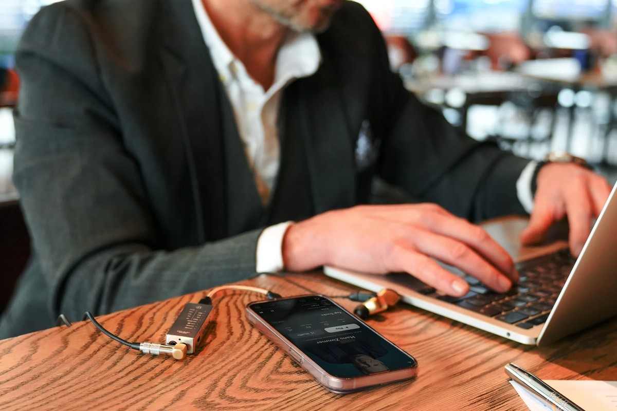 Man typing on a laptop on a terrace, phone and small DAC connected on the table