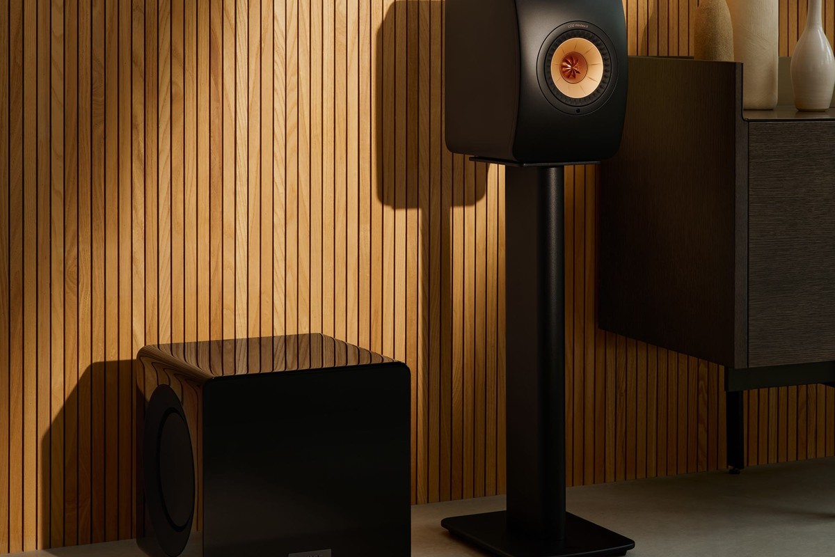 Caisson de basses KEF KC92 noir laqué au pied d'une enceinte, mur en bois