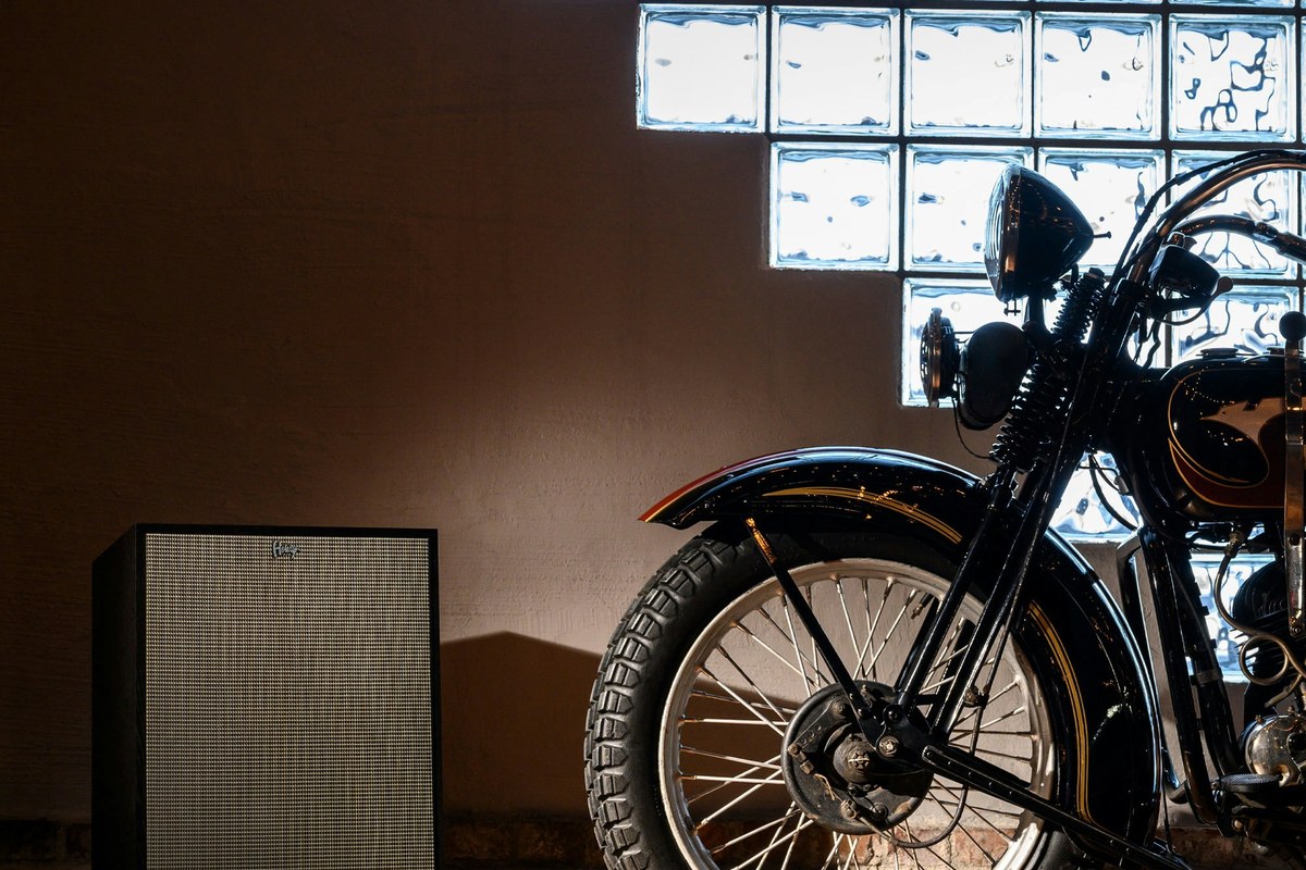 Enceinte noire avec grille posée au sol à côté d'une moto ancienne