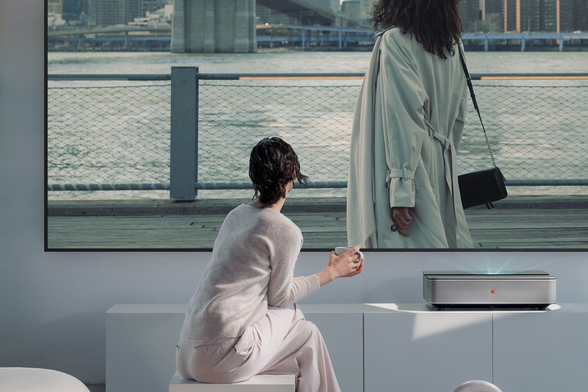 Laser projector on a low white cabinet, woman seated before the large image on the wall