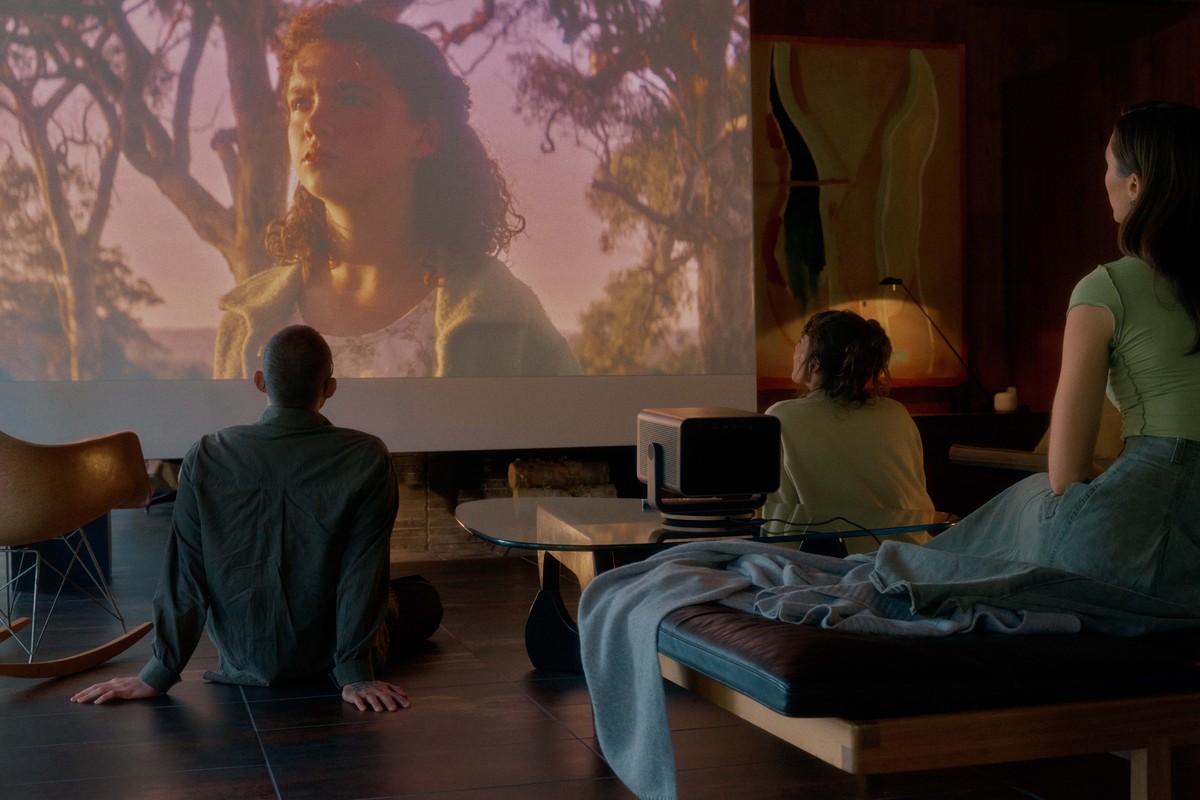 Small projector on a coffee table, film projected large on the wall in front of three people