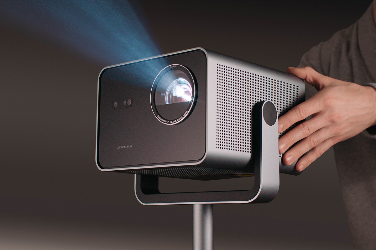 Close-up of a grey aluminium cube-shaped projector, a hand adjusting its tilt