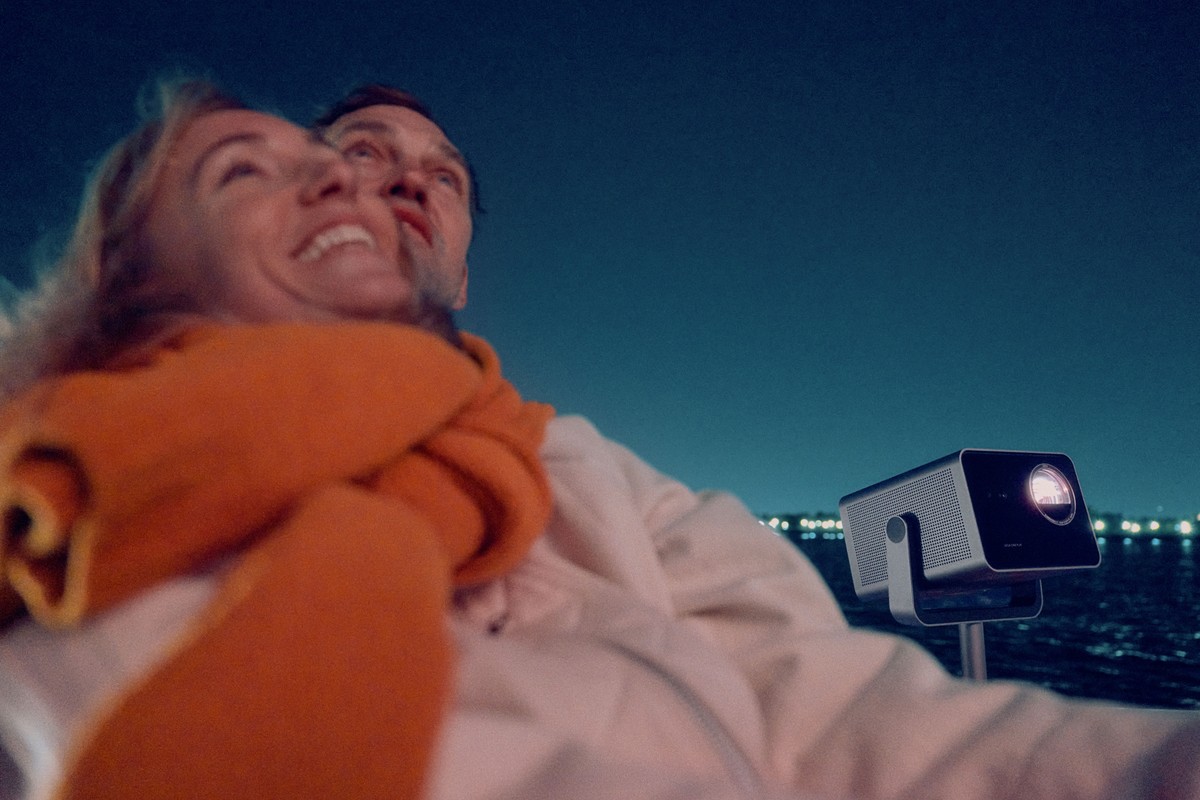 Projector on a floor stand outdoors, couple lying by the water at night