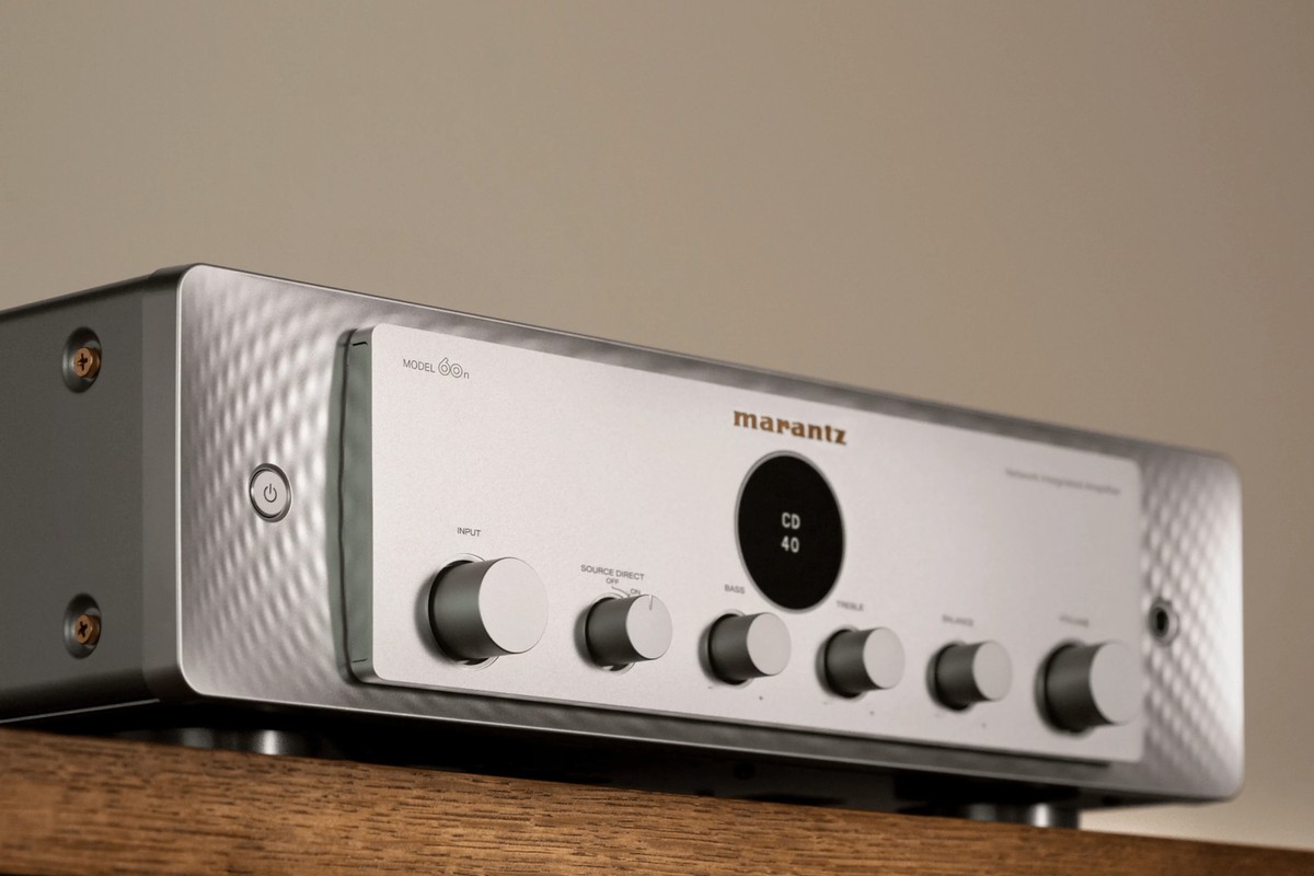 Vista di tre quarti di un frontale argento oro con display rotondo e pulsanti metallici, su un mobile in legno chiaro