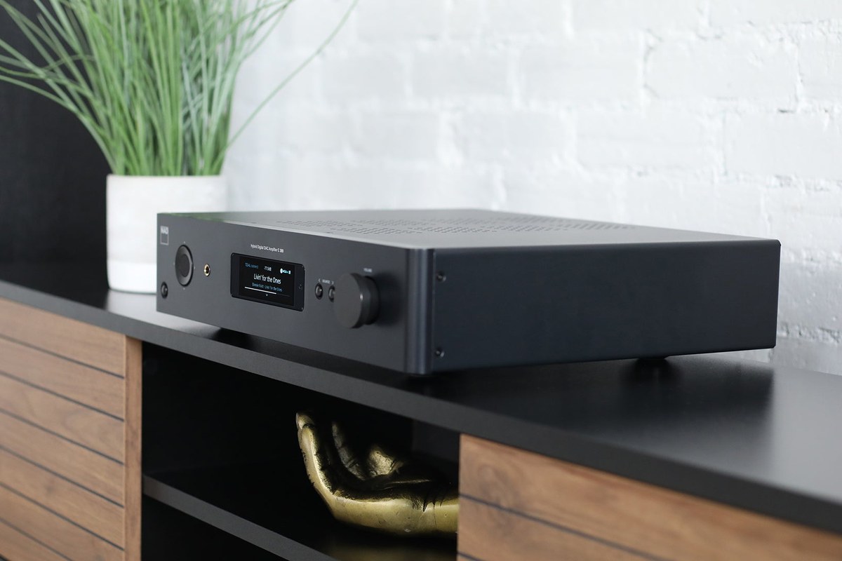 Amplificateur noir posé sur un meuble TV en bois, afficheur allumé