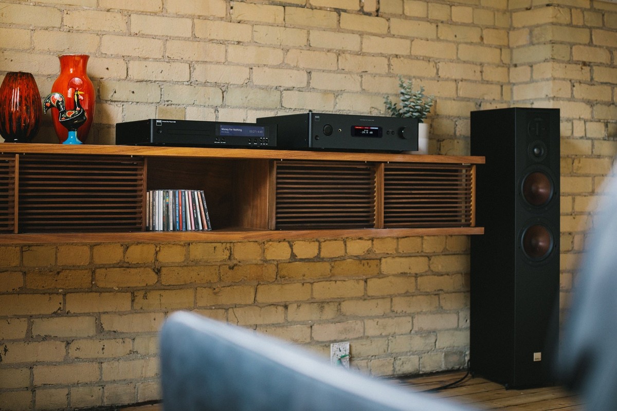 Lettore CD e amplificatore su una mensola in noce accanto a un diffusore da pavimento