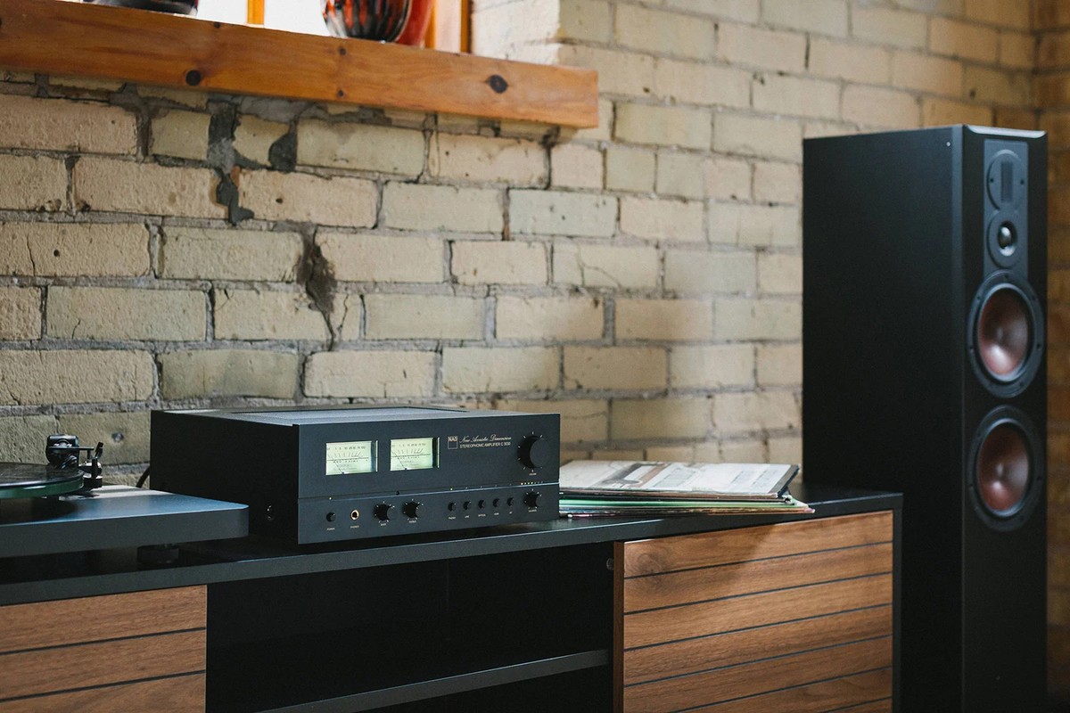 Amplificateur posé sur un meuble bas en bois, à côté d'une colonne et d'une platine vinyle