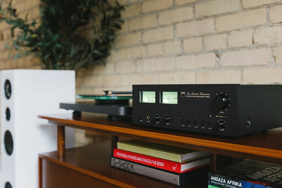 Amplificateur aux VU-mètres éclairés posé sur un meuble en bois, à côté d'une platine vinyle