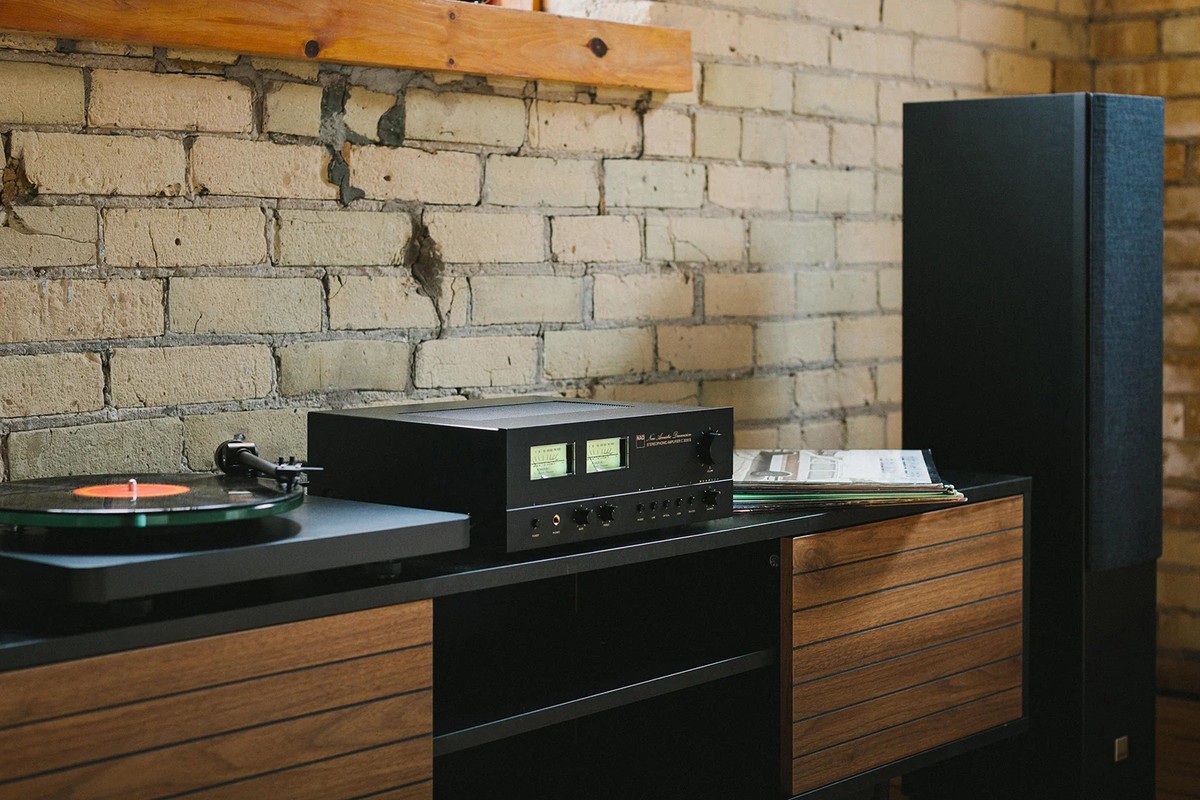 Amplificateur et platine vinyle sur un buffet en noyer, à côté d'une colonne noire