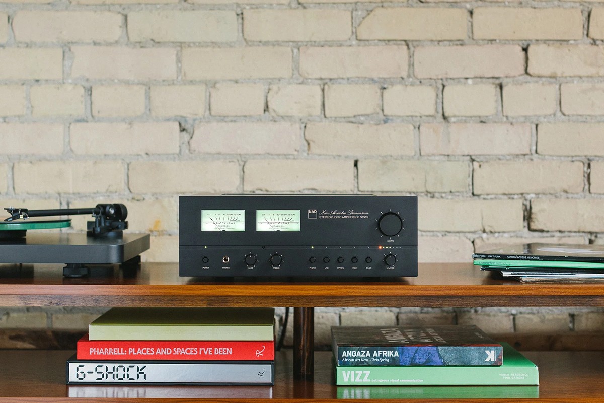 NAD C 3030S de face entre une platine vinyle et des disques, devant un mur de briques