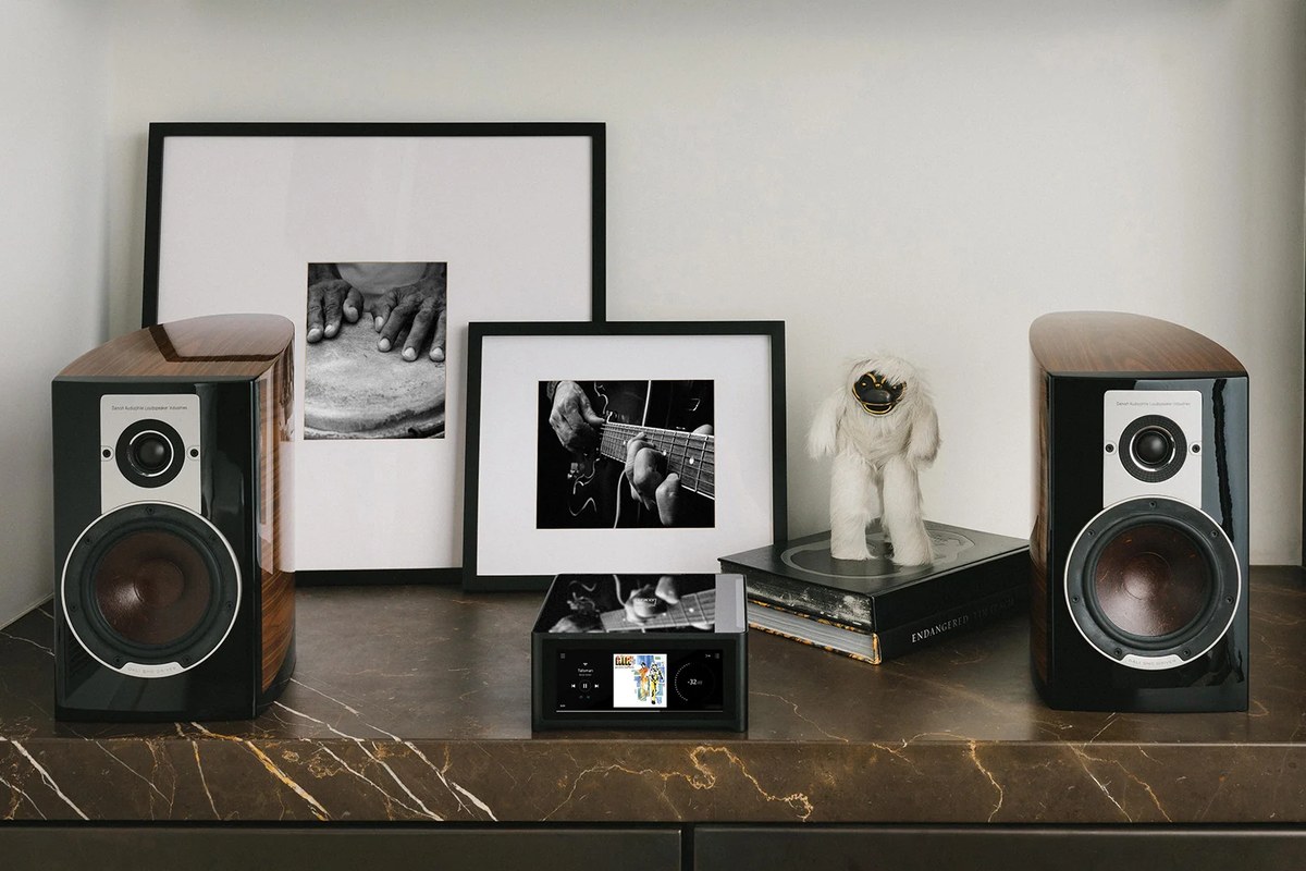 NAD M10 V3 zwischen zwei Kompaktlautsprechern auf einem Marmor-Sideboard