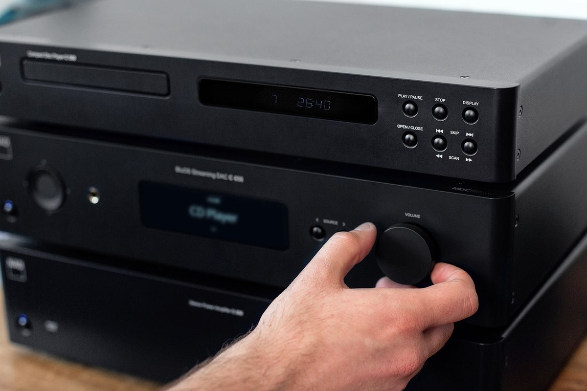 Black CD player on top of a streaming DAC whose volume knob is being turned