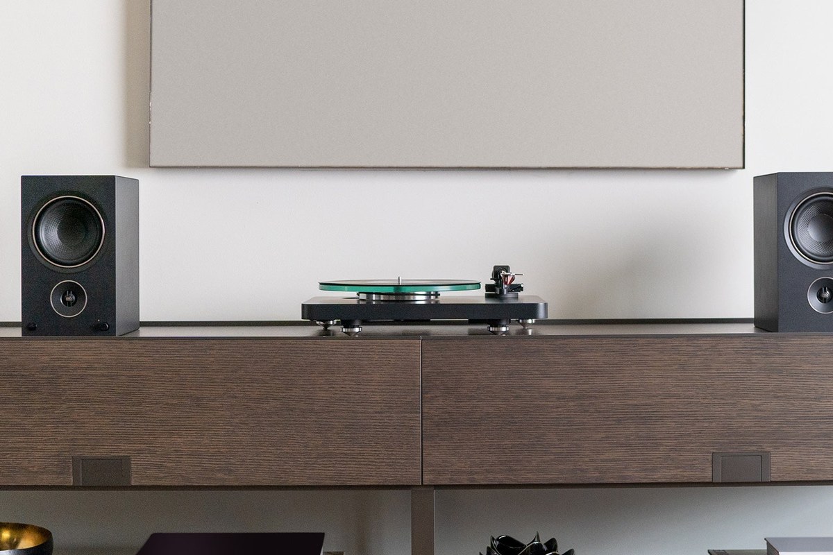 Turntable on a low cabinet between two speakers, below an acoustic panel