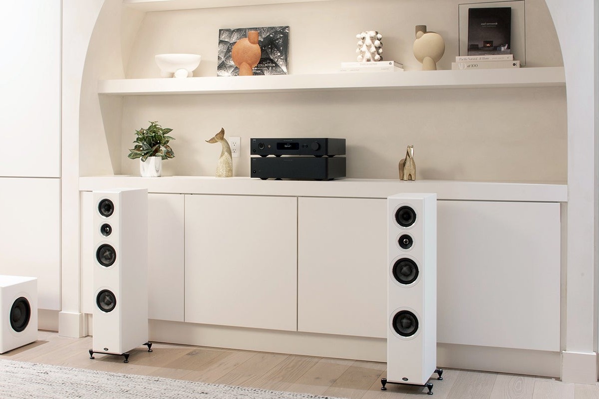 Bright living room with two white floorstanding speakers and NAD components on a shelf