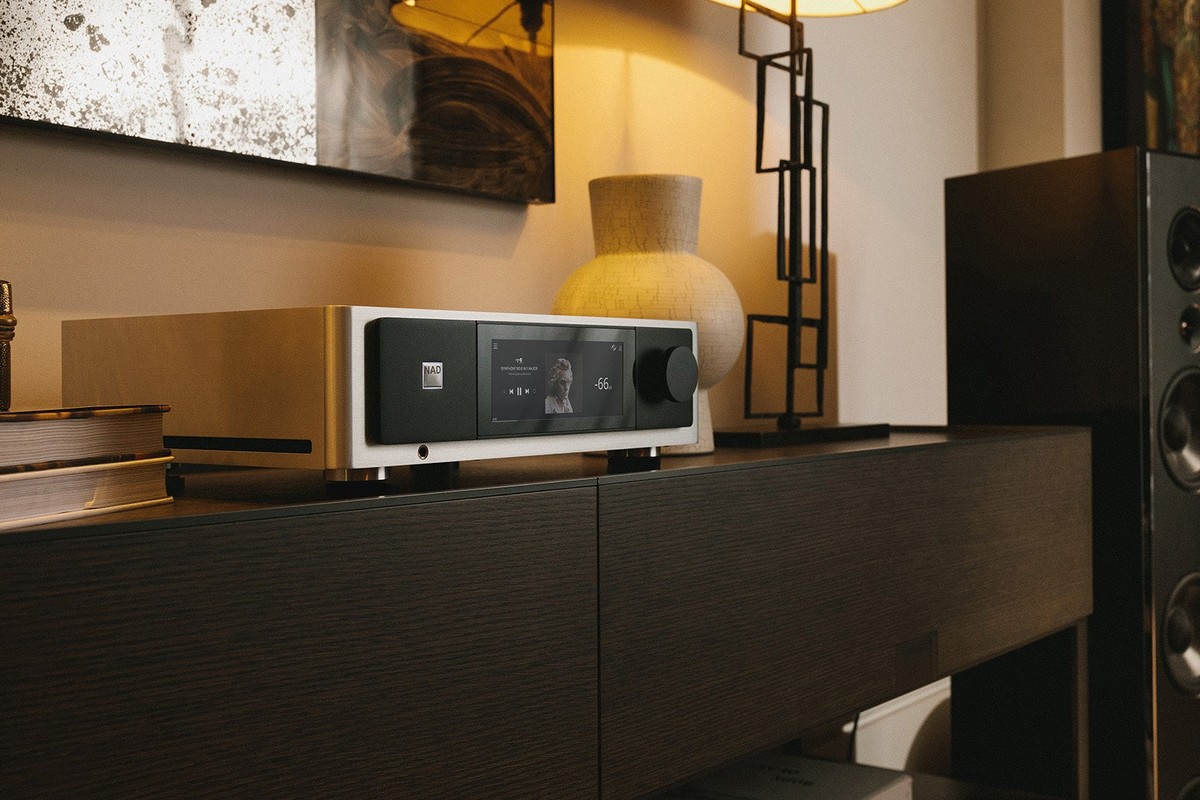 Amplificatore integrato su un mobile basso nero accanto a un diffusore da pavimento e a una lampada