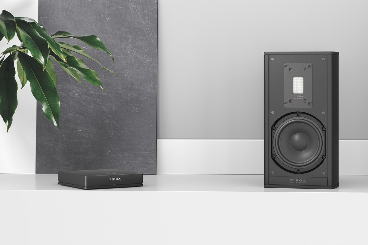 Module noir compact posé sur une étagère blanche à côté d'une enceinte compacte noire