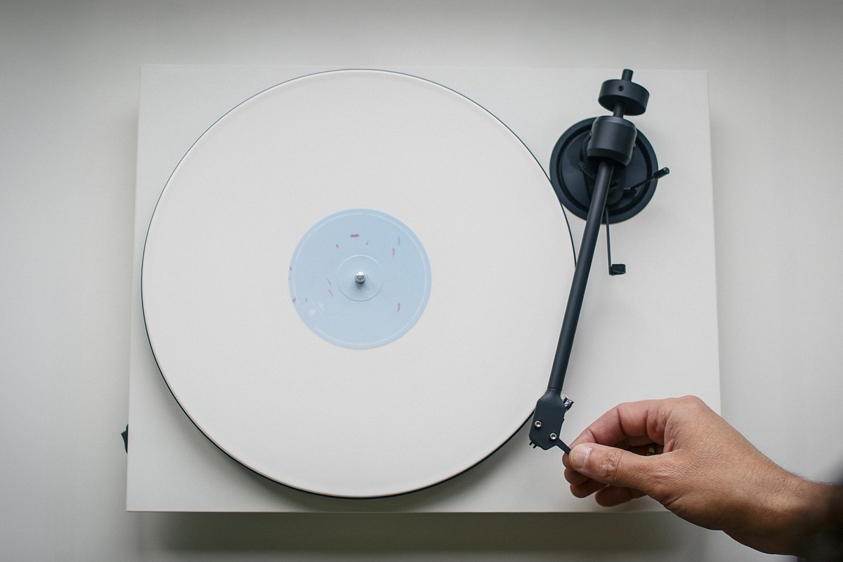Hand lifting the arm of a white turntable