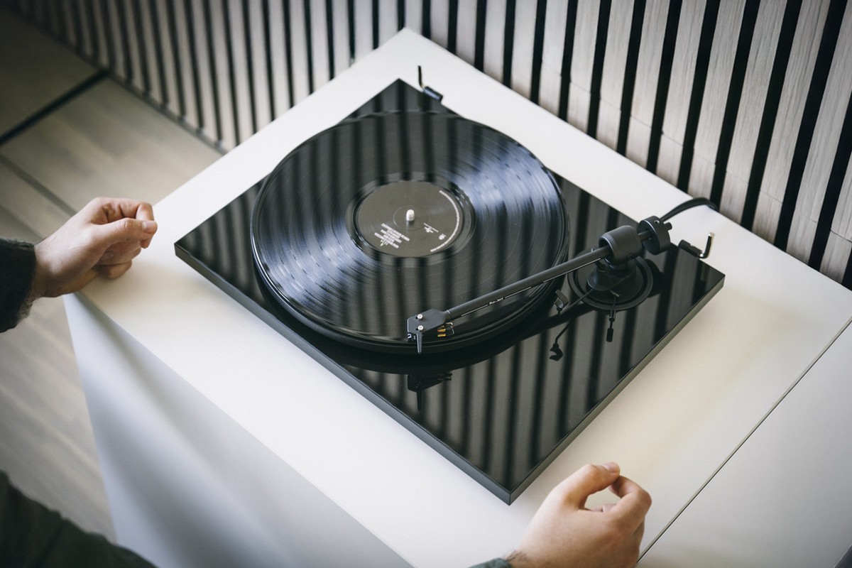 Hands setting up a black turntable on a white cabinet