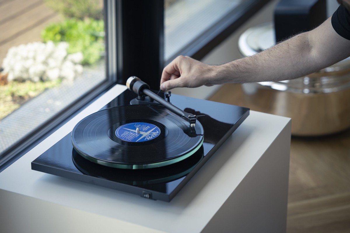 Main posant le bras sur un disque, platine noire près d'une fenêtre