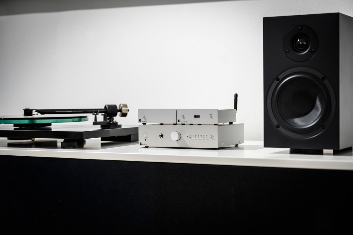 Préampli argent entre une platine vinyle et une enceinte noire