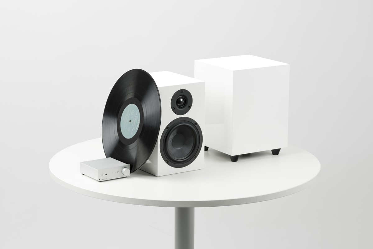 Subwoofer bianco su un tavolo rotondo accanto a un piccolo impianto per vinili