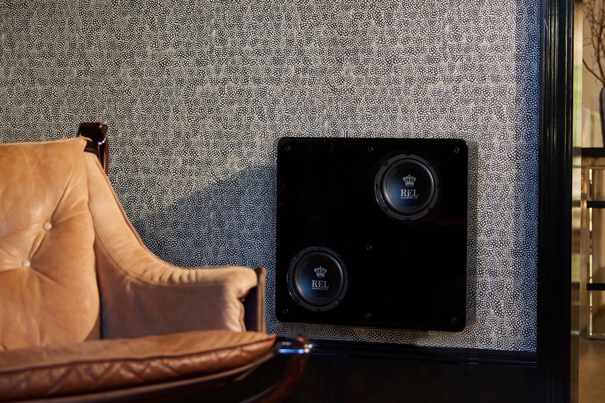 Flacher schwarzer Subwoofer an der Wand neben einem Ledersessel