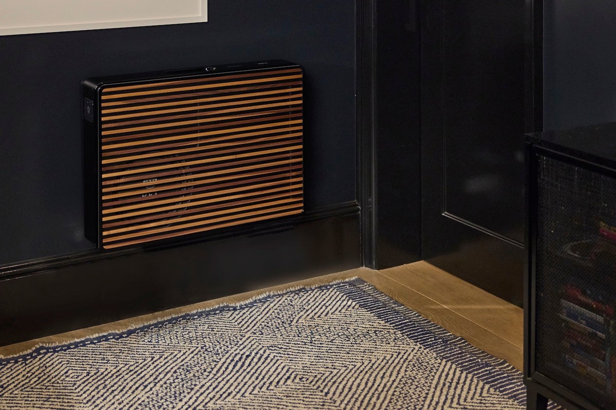 Slim black subwoofer with wooden grille against the wall of a dark living room