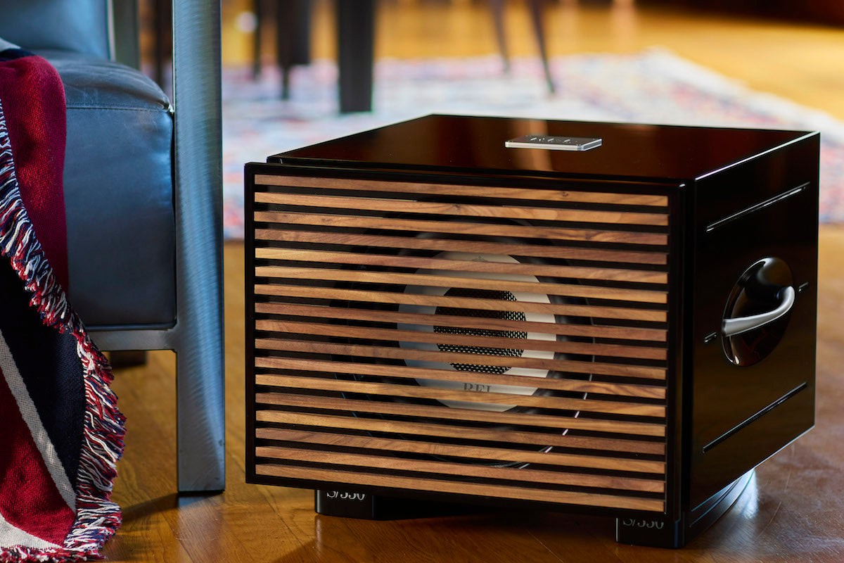 Schwarz lackierter Subwoofer mit Holzlamellen-Abdeckung auf dem Parkett eines Wohnzimmers