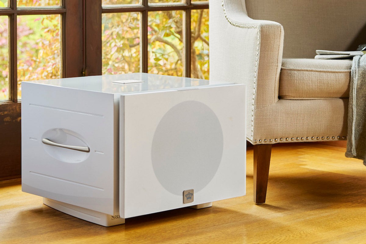Subwoofer bianco laccato con griglia in tessuto accanto a una poltrona, davanti a una finestra