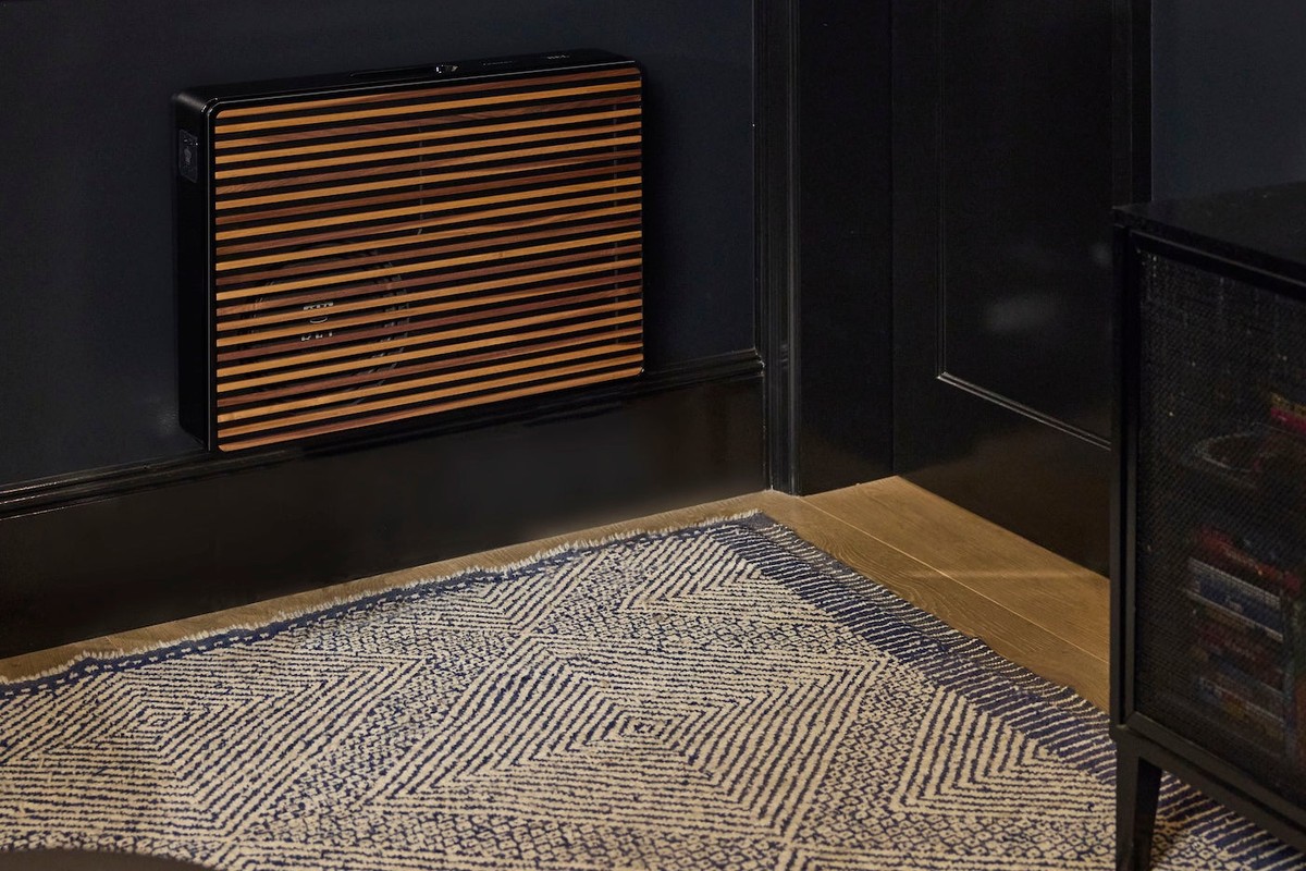 Black subwoofer with wood slats at the foot of a dark wall, on a rug